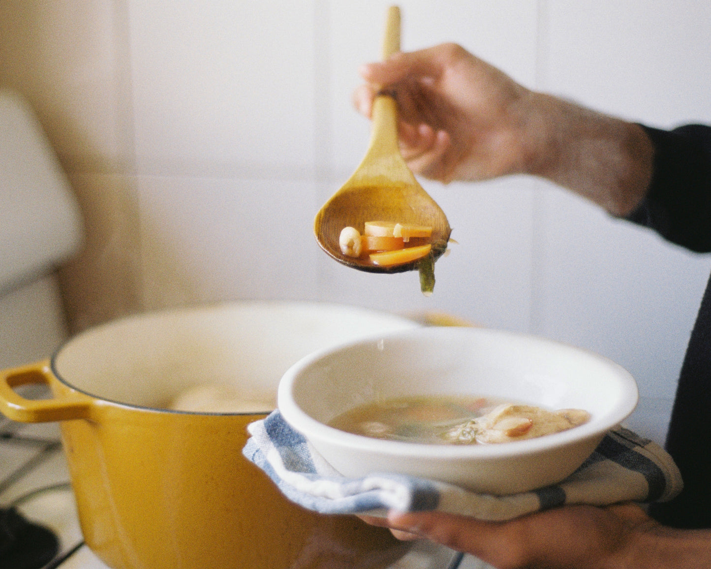 Man scooping herbal soup into a bowl from pot on stove in the kitchen
